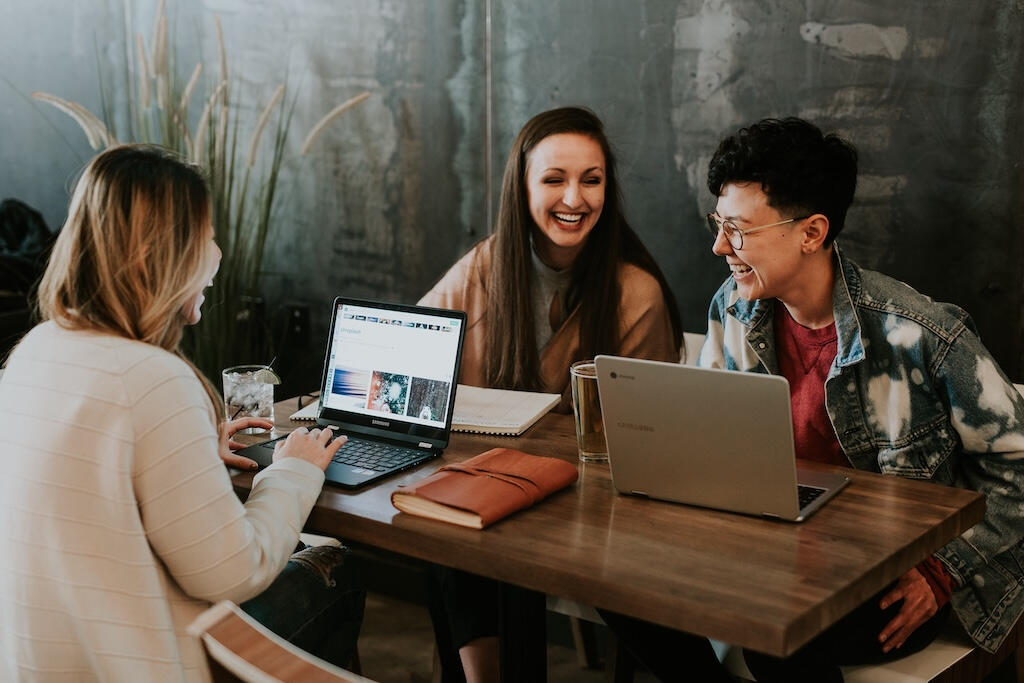 Three people sitting around a table with their computers open smiling and laughing