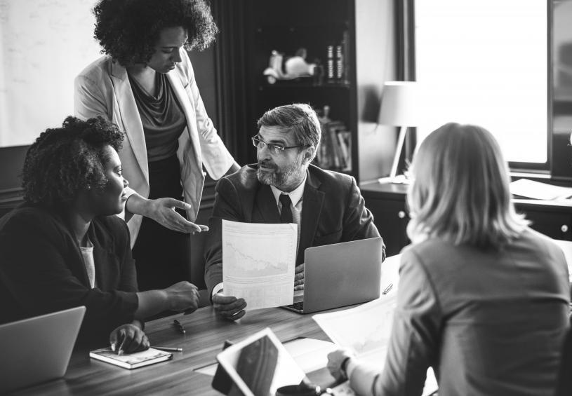 A professional woman handing a professional man an importance piece of paper around a conference table.